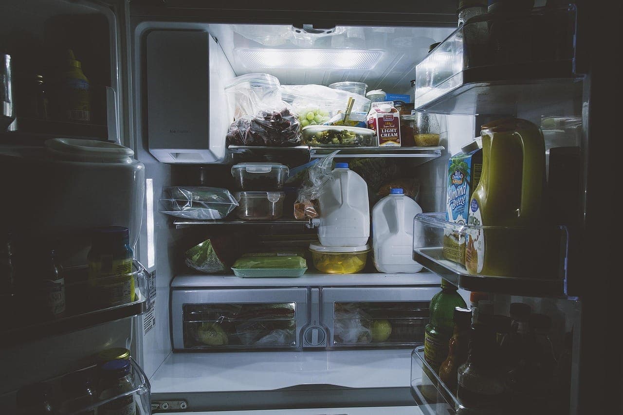 Открытый холодильник с продуктами светится в тёмной кухне